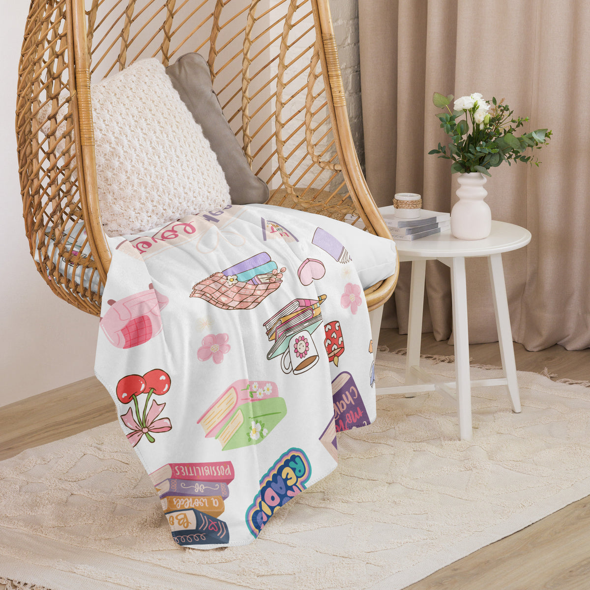A white sherpa blanket with bookish illustrations draped over a wicker chair.