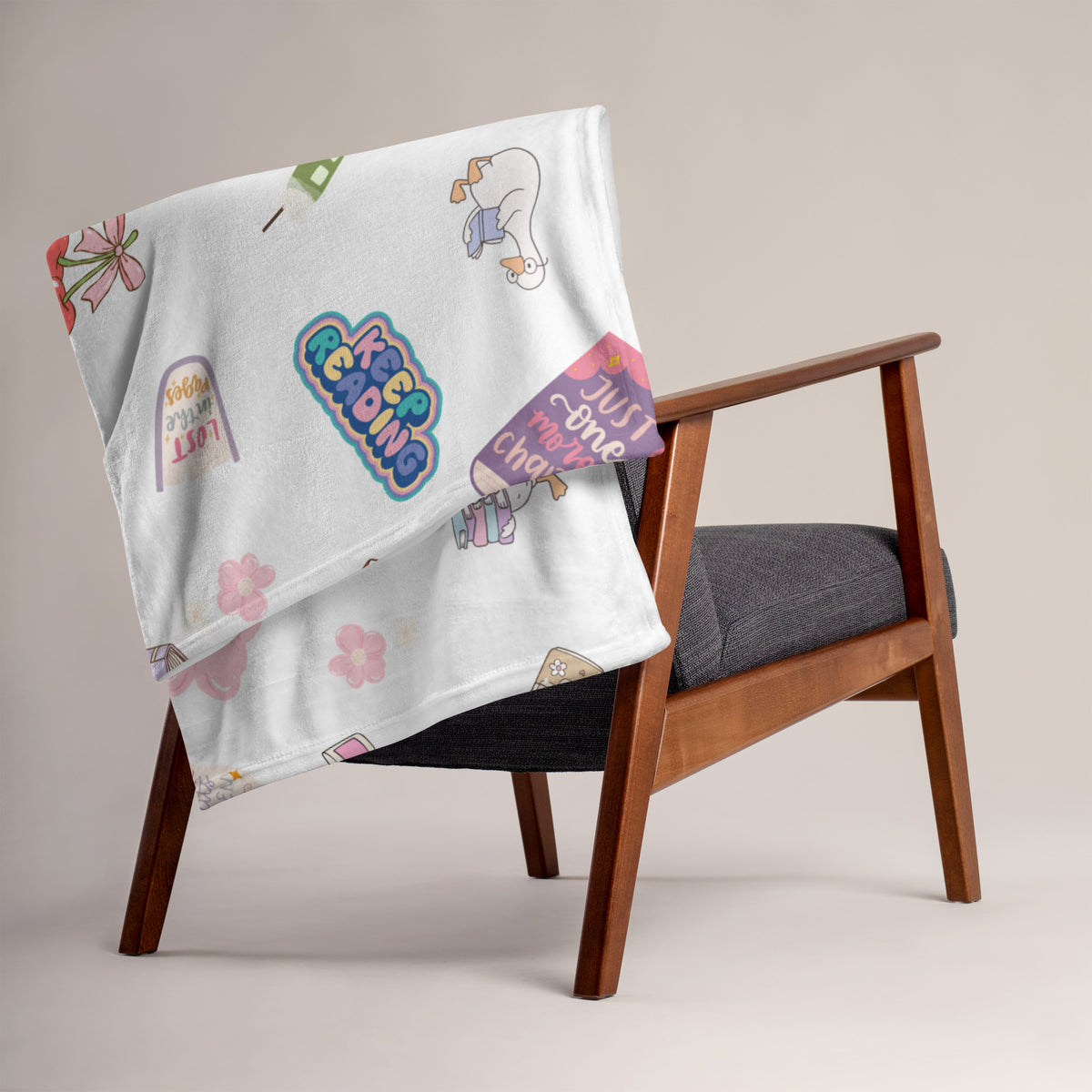 A white throw blanket with bookish illustrations is draped over a wooden chair.