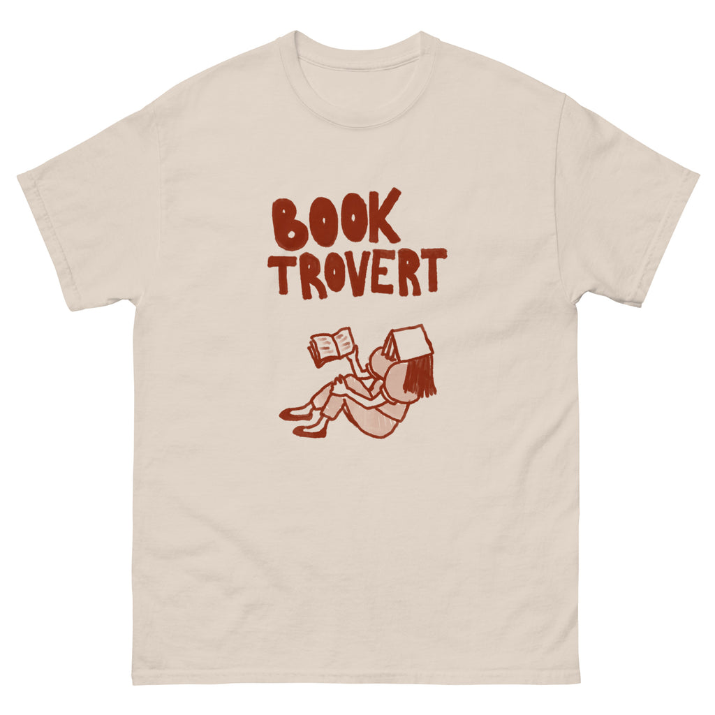 A cream t-shirt with a brown graphic of a person reading a book and the words "BOOK TROVERT".
