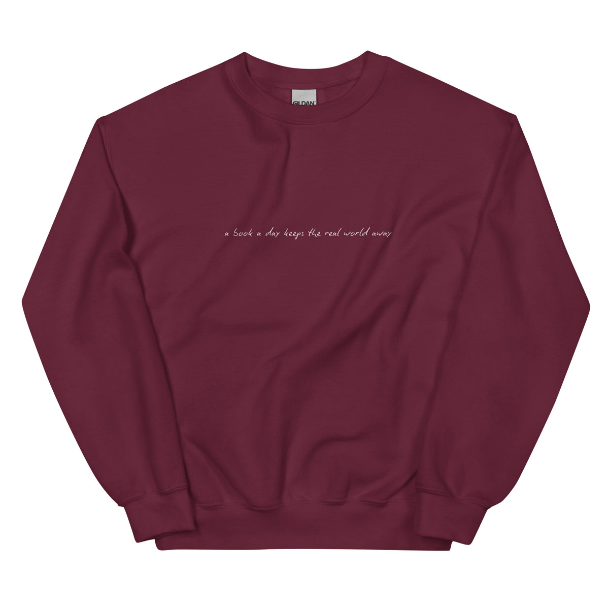 A maroon sweatshirt with the embroidered text "a book a day keeps the real world away".
