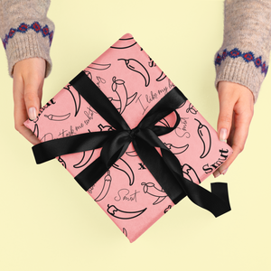 A pink gift box with chili pepper pattern and black ribbon is held by two hands.