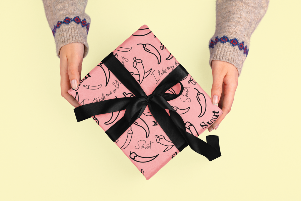 A pink gift box with chili pepper pattern and black ribbon is held by two hands.