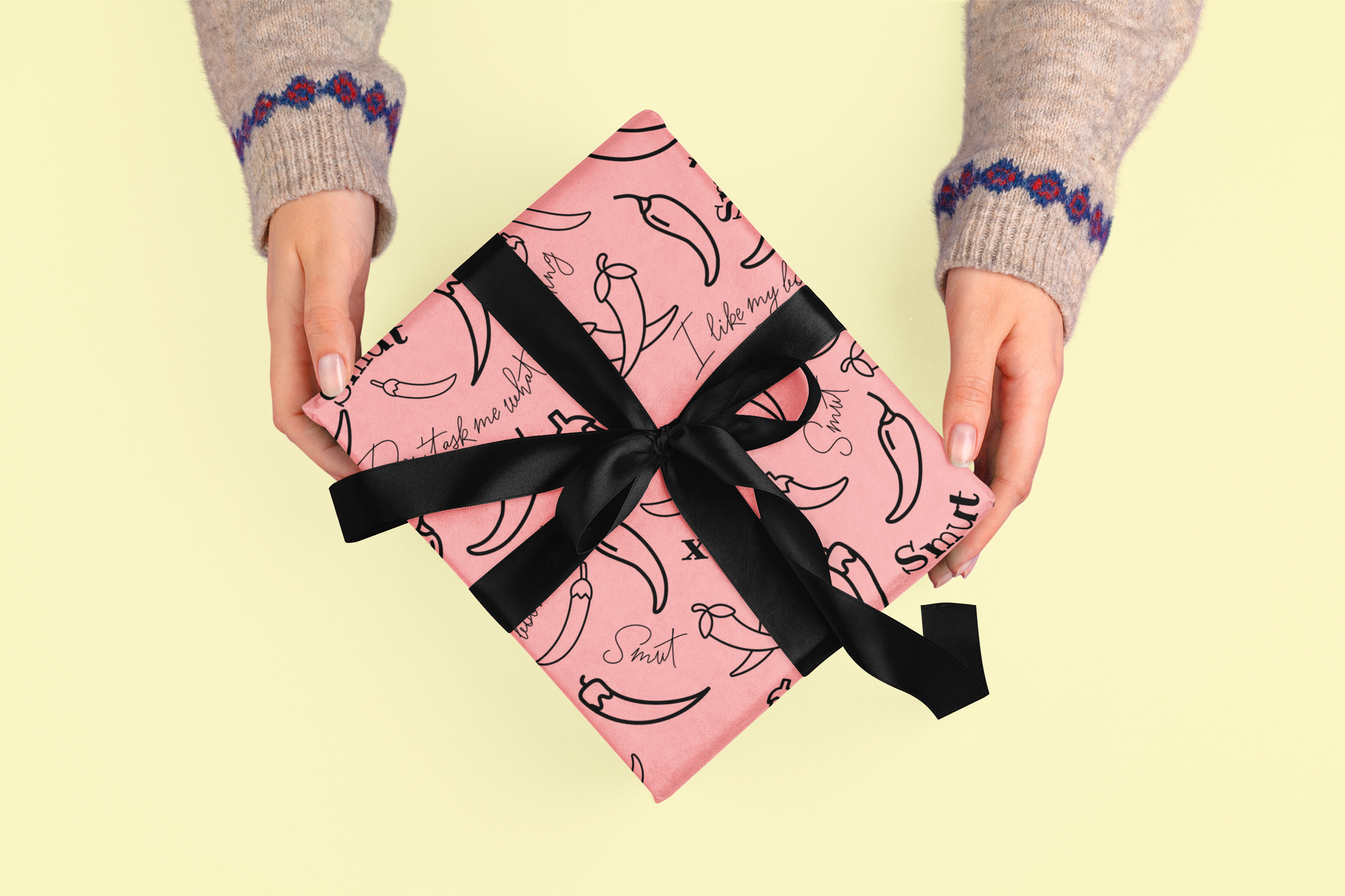 A pink gift box with chili pepper pattern and black ribbon is held by two hands.
