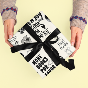 A gift wrapped in black and white paper with book-themed illustrations and a black ribbon.