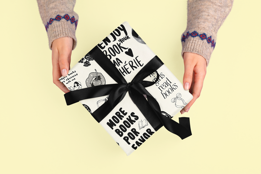 A gift wrapped in black and white paper with book-themed illustrations and a black ribbon.