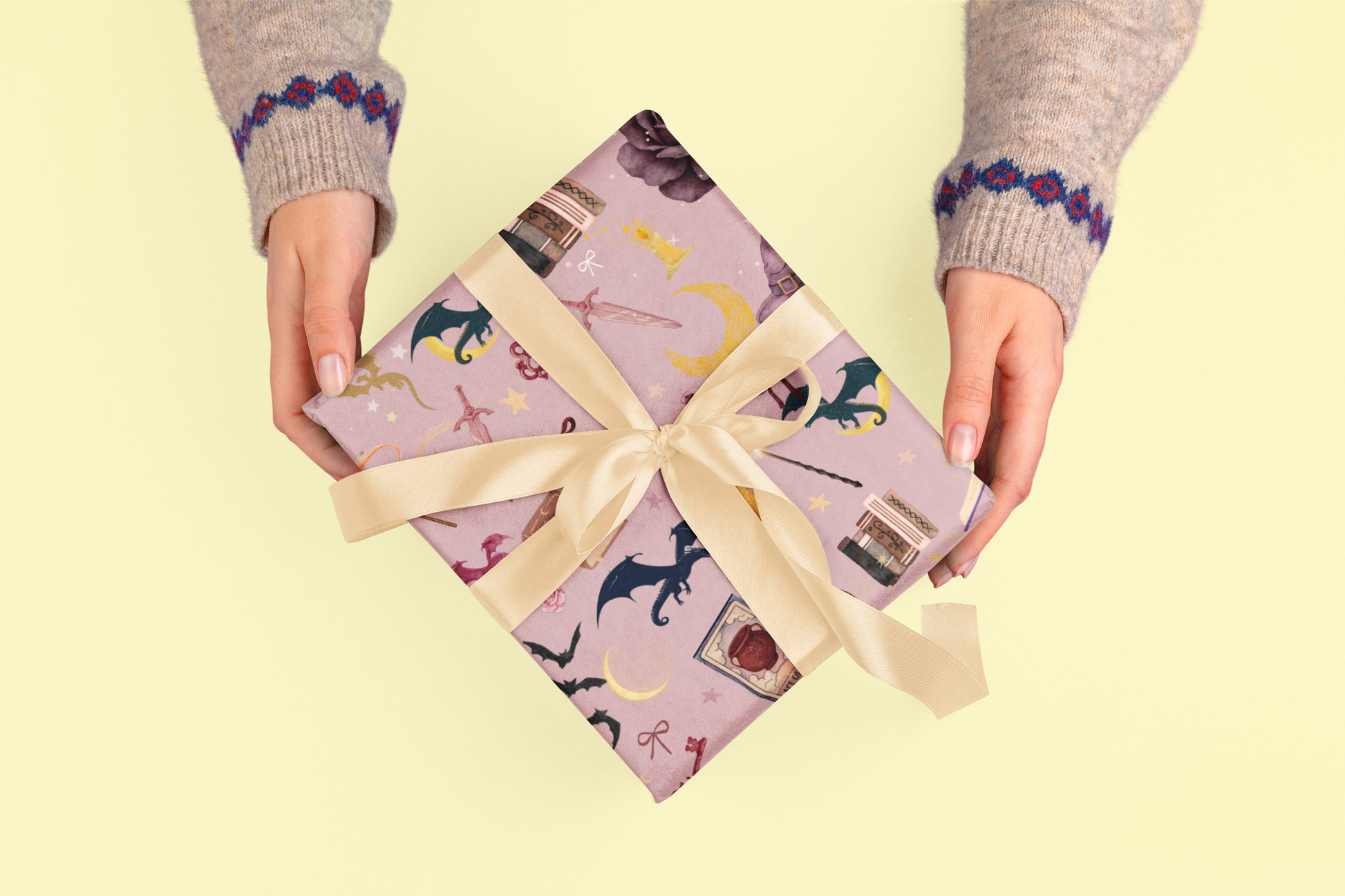Hands hold a gift wrapped in purple paper with fantasy illustrations and a gold ribbon.