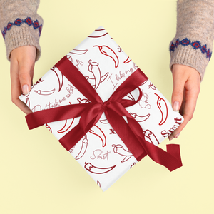 A gift wrapped in paper with red chili peppers and text, held by two hands.